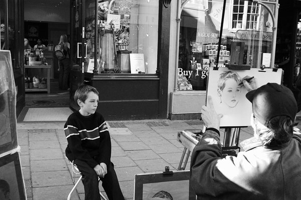 A boy sits for a street artist who is drawing his portrait on an easel
