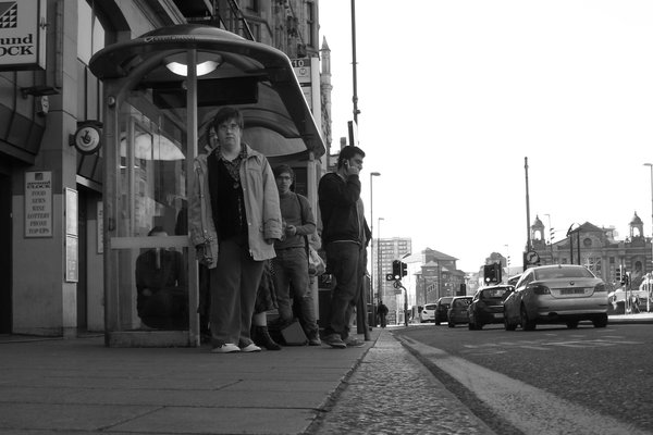 People wait at a bus shelter, seen from kerb level