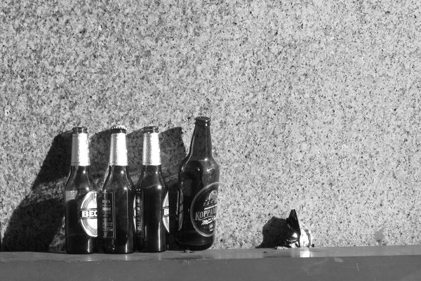 Four bottles and a crumpled packet in hard sunlight against a granite wall