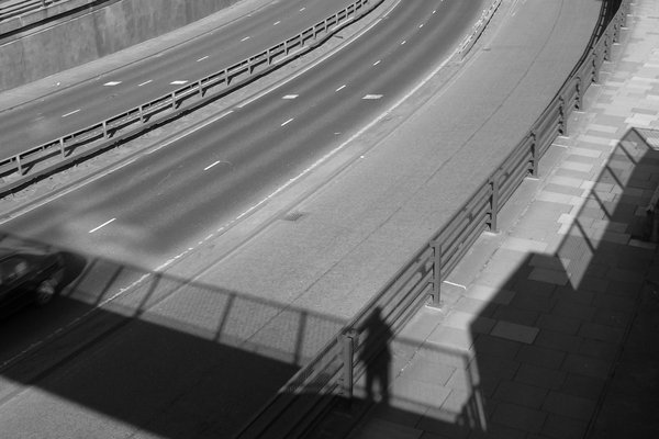 A curving road leading to an underpass, with a shadow figure at the railing