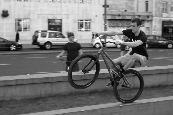 A rider lifts his front wheel on a stone ledge with the background blurred by panning