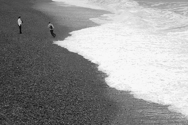 Two small figures on a pebble beach beside breaking surf